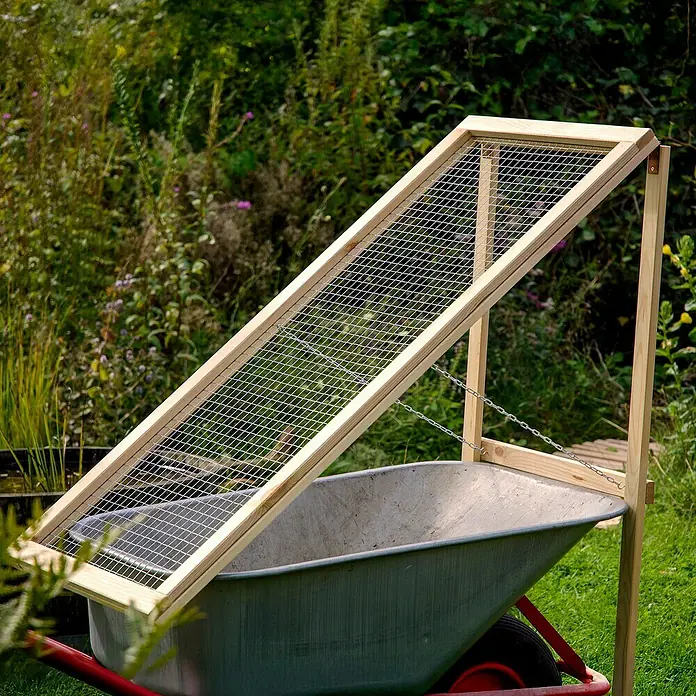 Dobar Durchwurfsieb - 53 x 110 x 85 cm, Holz - Detailansicht eines Gartensiebs aus Holz und Metall, das auf einer Schubkarre platziert ist, ideal für Gartenarbeiten.