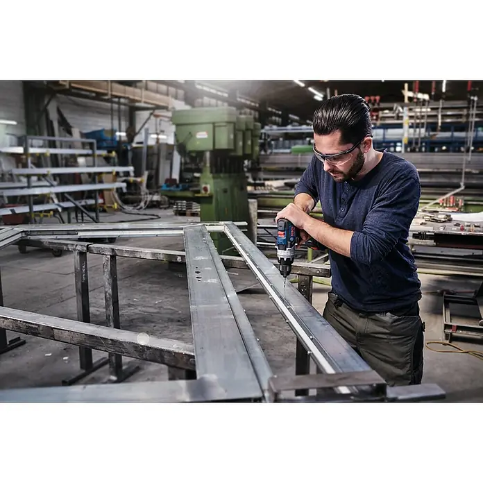 Bosch Metallbohrer PointTeQ - Durchmesser Bohrer: 10 mm - Mann mit Schutzbrille bohrt mit einem Bosch-Akkuschrauber Löcher in ein Metallstück in einer Werkstatt.