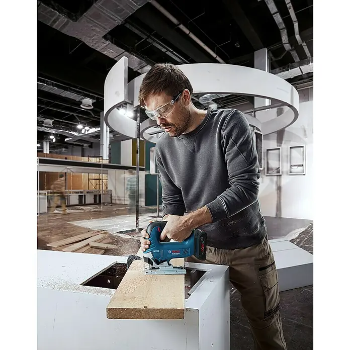 Bosch Professional AMPShare 18V Akku-Pendelhubstichsäge GST 18V-125 B - 18 V, Ohne Akku, Leerlaufhubzahl: 0 /min - 3.500 /min - Mann arbeitet mit einer Bosch Stichsäge an einem Holzstück. Die blaue Akku-Stichsäge ist ein hochwertiges Werkzeug für präzise Holzarbeiten.