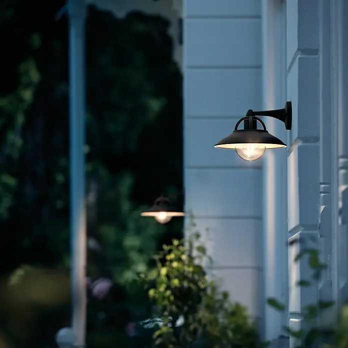 Philips Aplique exterior Cormorant - 42 W, 265 x 250 x 218 mm, Negro, IP44 - Esta foto muestra una lámpara de pared exterior clásica con un brillo cálido, creando un ambiente acogedor para el exterior.
