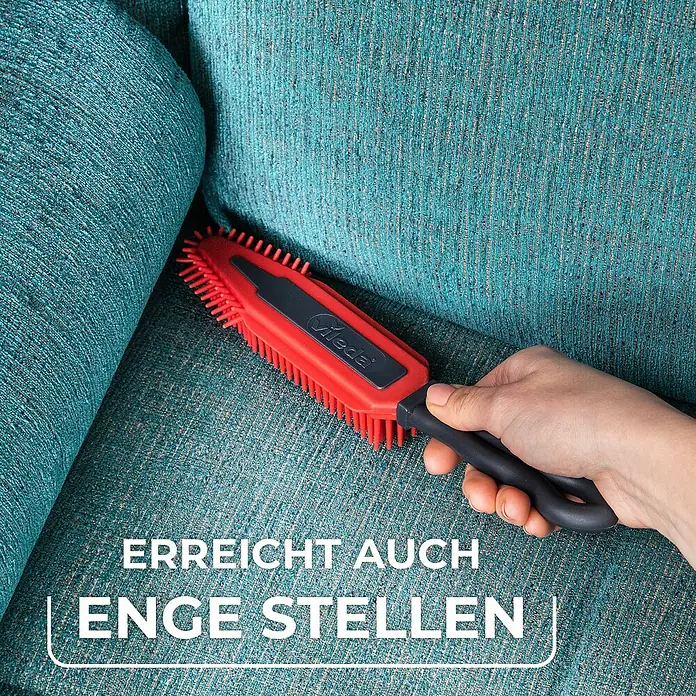 Vileda pet pro Tierhaar-Entferner Electrostatic Brush - Rot/Schwarz, Material Borsten: Gummi, Kunststoff - Nahaufnahme einer Hand, die eine Vileda Bürste auf einem türkisfarbenen Sofa verwendet, um schwer zugängliche Stellen zu reinigen.