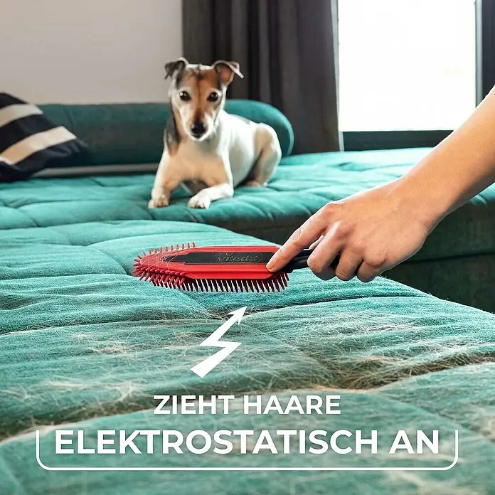 Vileda pet pro Tierhaar-Entferner Electrostatic Brush - Rot/Schwarz, Material Borsten: Gummi, Kunststoff - Das Bild zeigt eine Vileda Fusselbürste in Aktion auf einer Couch, um Tierhaare elektrostatisch anzuziehen, während ein Hund zusieht.