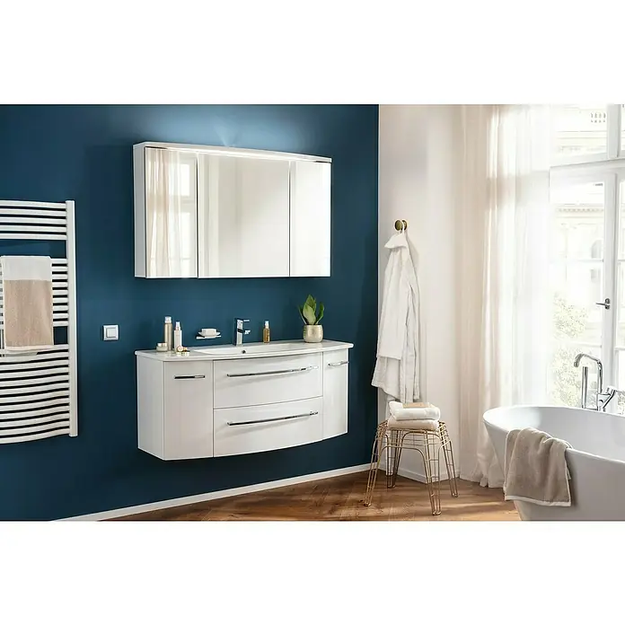 Camargue Swing K Waschtischunterschrank - B x T x H: 119 x 45,9 x 51,8 cm, Weiß, Farbe Griff: Chrom - Elegantes Badezimmer-Interieur mit einem stilvollen weißen Waschtisch mit Spiegel und einem Handtuchwärmer an der blauen Wand.