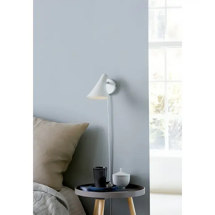 Nordlux Vanila Aplique de pared - 40 W, L x An x Al: 14,5 x 14,5 x 17 cm, Blanco, E14 - Un aplique de pared blanco con una pantalla cónica está montado sobre una mesita de noche con una taza y un bote.
