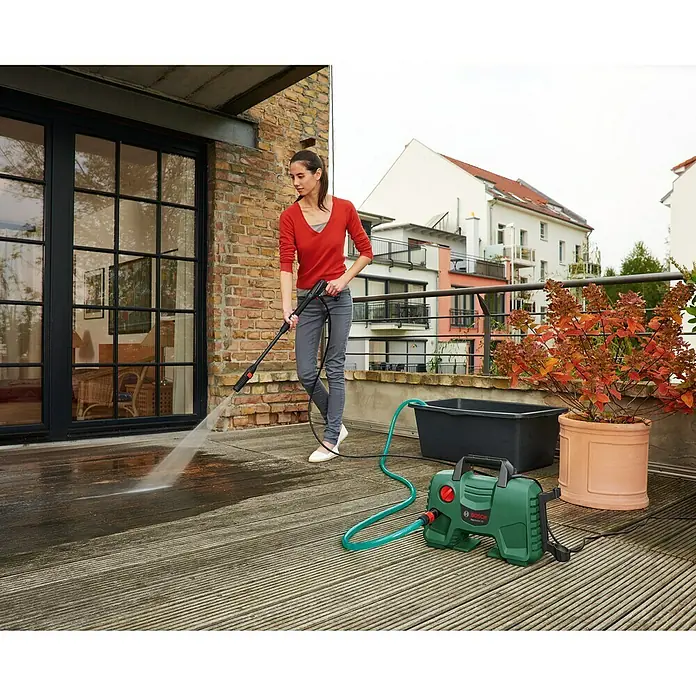 Bosch Hochdruckreiniger EasyAquatak 120 - 1.500 W - Frau reinigt Terrasse mit einem Bosch Hochdruckreiniger, der auf dem Boden steht und mit einem Schlauch verbunden ist.
