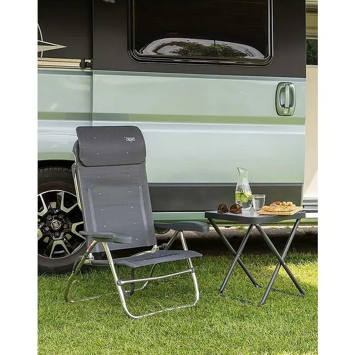 Crespo Tischplatte M/201 - L x B x H: 42 x 42 x 3,5 cm, Melamin/Aluminium - Ein grauer Campingstuhl mit einem kleinen Tisch daneben, auf dem sich ein Getränk und Snacks befinden, vor einem Wohnmobil.