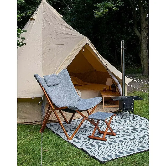 Bo-Camp Campingstuhl Bloomsbury - B x T x H: 75 x 87 x 96 cm, Grau/Braun, Holz/Polyestergewebe - Grauer Stuhl mit Hocker vor einem Glamping-Zelt und einem Outdoor-Ofen auf einer gemusterten Matte im Grünen.
