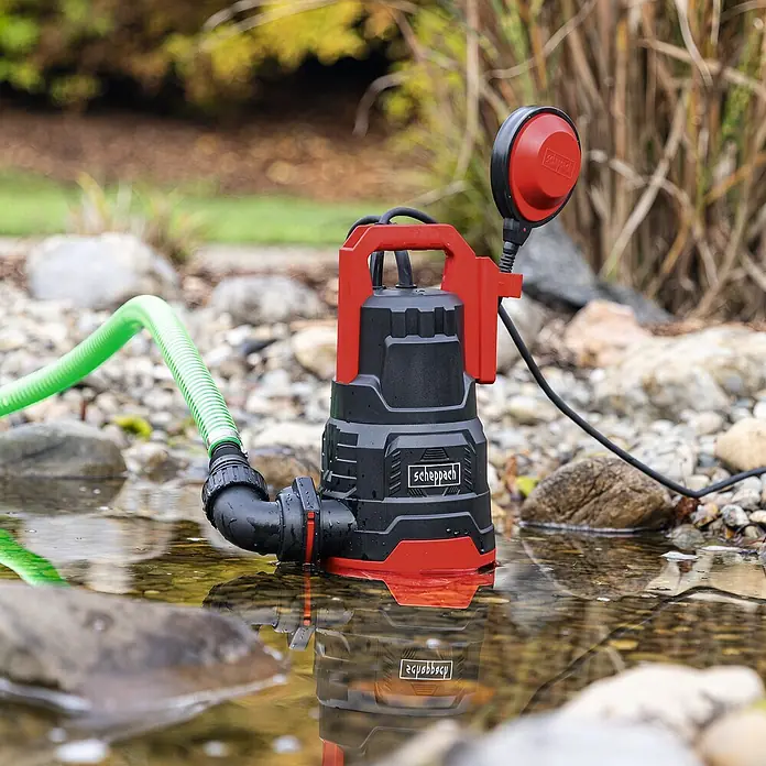 Scheppach Schmutzwasserpumpe DWP 400 - 400 W, Max. Fördermenge: 9.000 l/h, Eintauchtiefe: 7 m - Die Scheppach Tauchpumpe im Einsatz, umgeben von Wasser und Steinen, mit einem grünen Schlauch angeschlossen für effiziente Wasserförderung.