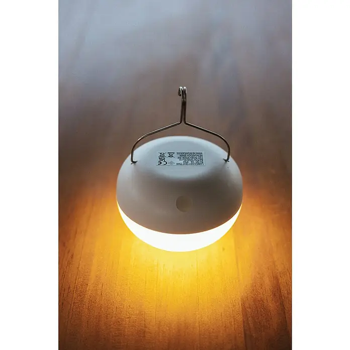 New Garden LED-Poolbeleuchtung Coco Floating Blulb - Durchmesser: 11 cm, Weiß, LED - Nahaufnahme einer leuchtenden, runden Lampe mit Aufhängevorrichtung auf einem Holztisch, die warmes Licht abstrahlt.