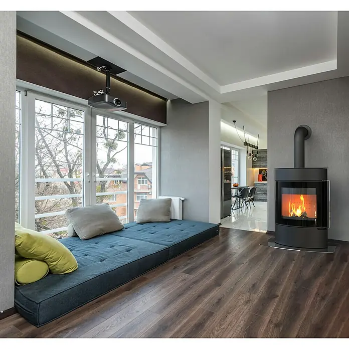 Kaminofen Elipso Max - 8 kW, Raumheizvermögen: 229 m³, Material Verkleidung: Stahl, Schwarz - Gemütliches Wohnzimmer mit blauem Fensterbett, Kaminofen und Projektor für entspannte Filmabende. Der Holzboden rundet das Ambiente ab.