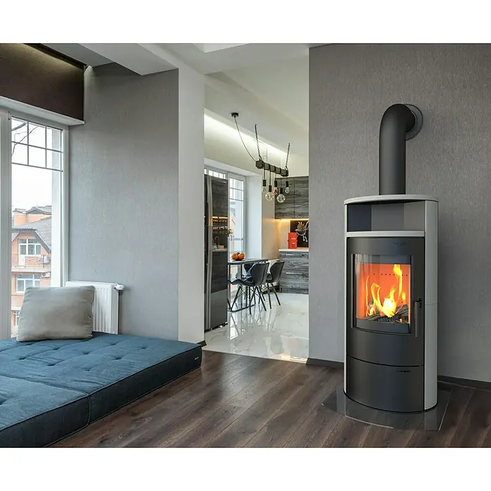 Kaminofen Cumulus Limestone - 7 kW, Raumheizvermögen: 200 m³, Schwarz - Moderner Kaminofen mit loderndem Feuer, elegantem Design in Schwarz und Weiß, und einem Rohr an der grauen Wand.