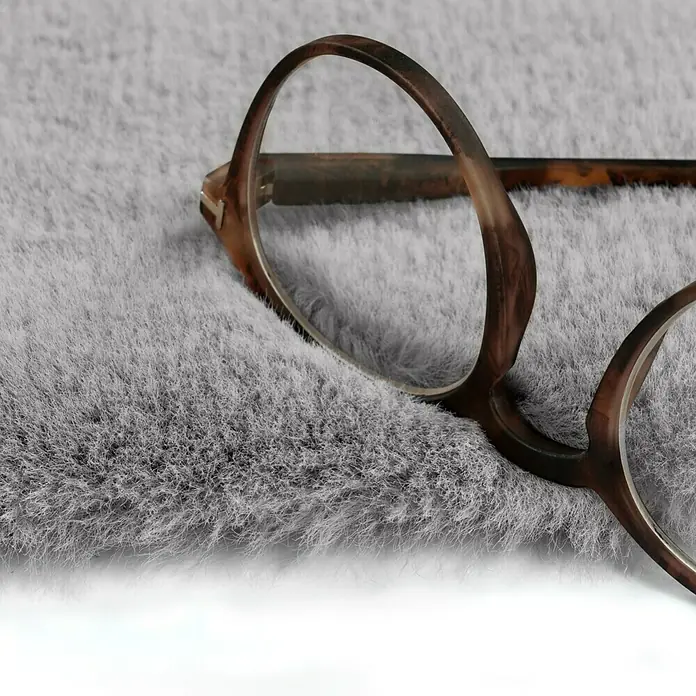 Fellteppich Happy - Silber, 330 x 240 cm, 100 % Polyester (Flor) - Nahaufnahme einer eleganten, braunen Brille auf einem weichen, grauen Tuch. Die Brille hat klare Gläser und ein stilvolles Design.