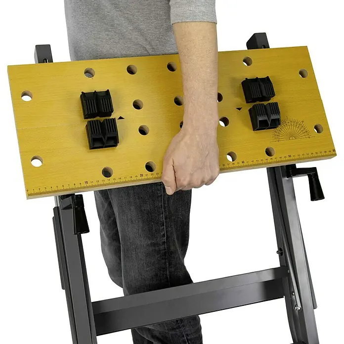 Werkbank Klappbar - L x B: 63,5 x 60,6 cm, Arbeitshöhe: 76 cm, Belastbarkeit: 150 kg - Eine gelbe Werkbank mit schwarzen Spannbacken und einer Metallschiene, die von einer Person gehalten wird.