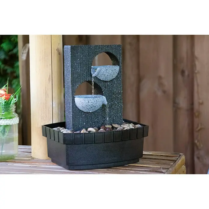 Dobar Gartenbrunnen - 20,5 x 16,5 x 26 cm, Kunststoff, Grau/Schwarz - Nahaufnahme eines dekorativen Zimmerbrunnens mit zwei Schalen, aus denen Wasser in ein Becken mit Kieselsteinen fließt.