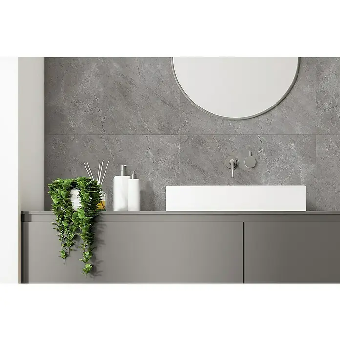 Inspiro Revestimiento de pared de PVC Twilight - 75 x 45 cm, Gris - Primer plano de un baño moderno con lavabo, grifo, espejo y planta en una estantería gris sobre una pared de piedra gris.