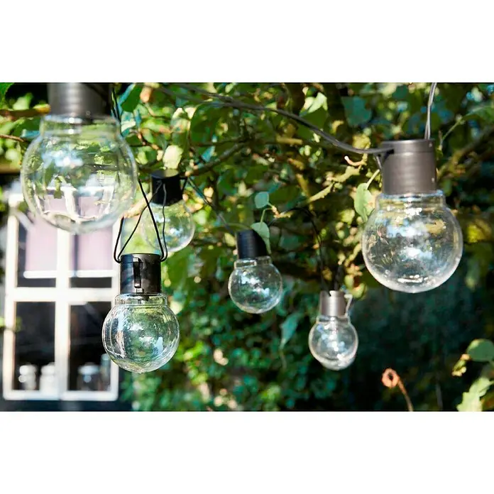 Luxform Guirnalda luminosa solar Menorca - Largo: 349 cm, LED - Primer plano de una serie de bombillas transparentes de exterior colgadas en un exuberante jardín verde.