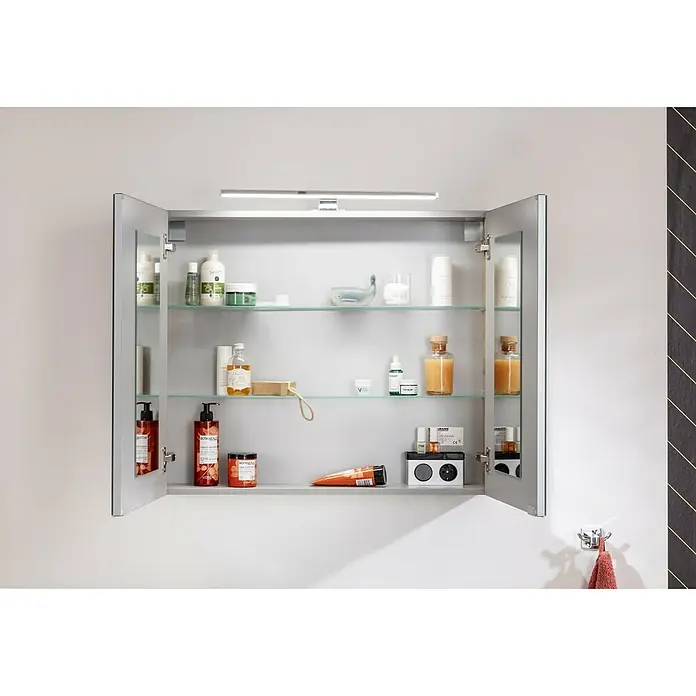 Fackelmann B.brillant LED-Spiegelschrank - B x H: 80 x 68 cm, 2-türig, Ast Eiche - Ein offener Spiegelschrank mit diversen Pflegeprodukten auf Glasböden, beleuchtet von einer schlanken Lampe.