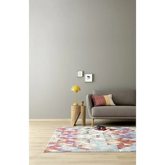 SCHÖNER WOHNEN-Farbe Wandfarbe Designfarbe - Dynamisches Platingrau, Matt, 2,5 l, Konservierungsmittelfrei - Eine stilvolle Inneneinrichtung mit einem bunten Teppich, einem grauen Sofa und einer gelben Lampe auf einem Holztisch.