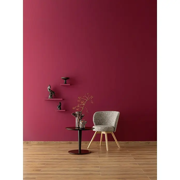 SCHÖNER WOHNEN-Farbe Wandfarbe Designfarbe - Gefühlvolles Herzensrot, Matt, 100 ml, Konservierungsmittelfrei - Einrichtungsidee mit einem stilvollen Tisch, einer Vase und einem bequemen Stuhl vor einer eleganten, bordeauxroten Wand.