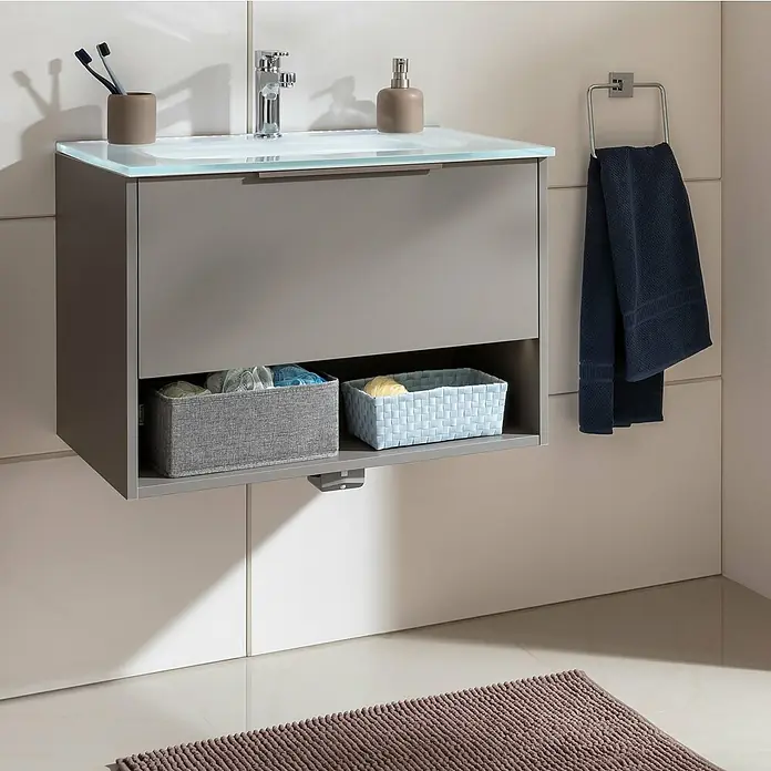 Fackelmann B.Paris Badmöbel-Set - Gesamtbreite Badmöbel: 70,5 cm, Cubanit grau, Waschbecken aus Glas - Grauer Badezimmerschrank mit Glasplatte, Armatur und zwei Körben auf einem beigen gefliesten Boden. Handtuchhalter mit blauem Handtuch ist auch zu sehen.