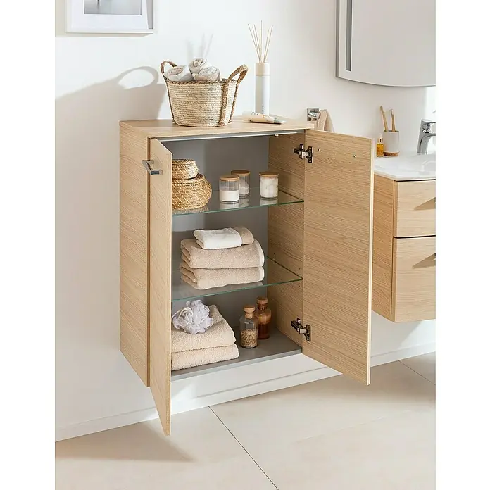 Fackelmann B.style Midischrank - 2-türig, B x T x H: 60,2 x 32 x 82,6 cm, Sandeiche - Ein offener Badezimmerschrank in hellem Holzton mit Glasböden, gefüllt mit Handtüchern und Badutensilien.