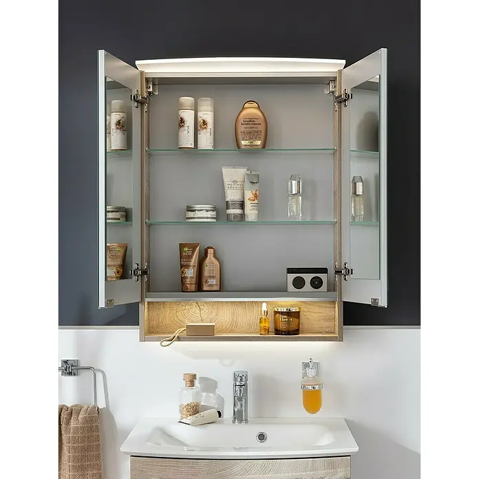 Fackelmann B.style LED-Spiegelschrank - B x H: 60 x 81,2 cm, Nature Oak Holzoptik - Ein offener Badezimmerschrank mit Glasböden und verschiedenen Pflegeprodukten, beleuchtet, über einem Waschbecken montiert.