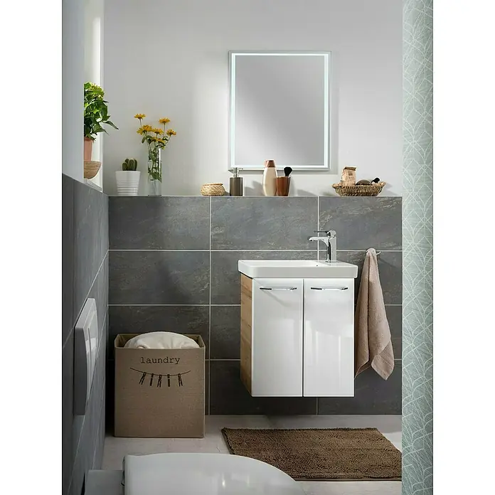 Fackelmann Milano Waschbeckenunterschrank - B x T x H: 520 x 275 x 610 mm, Ast Eiche, Weiß - Ein modernes Badezimmer mit einem beleuchteten Spiegel, einem Waschbeckenunterschrank und einer Wäschebox. Die grauen Fliesen und Akzente verleihen dem Raum Eleganz.