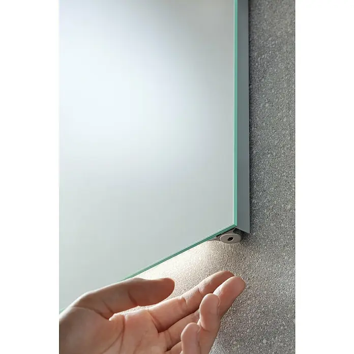 Fackelmann Lichtspiegel Mirror - B x H: 60 x 75 cm, Sensorschalter, Ambientebeleuchtung - Nahaufnahme eines modernen Spiegels mit LED-Beleuchtung an einer strukturierten Wand, der einen eleganten und funktionalen Designaspekt hervorhebt.