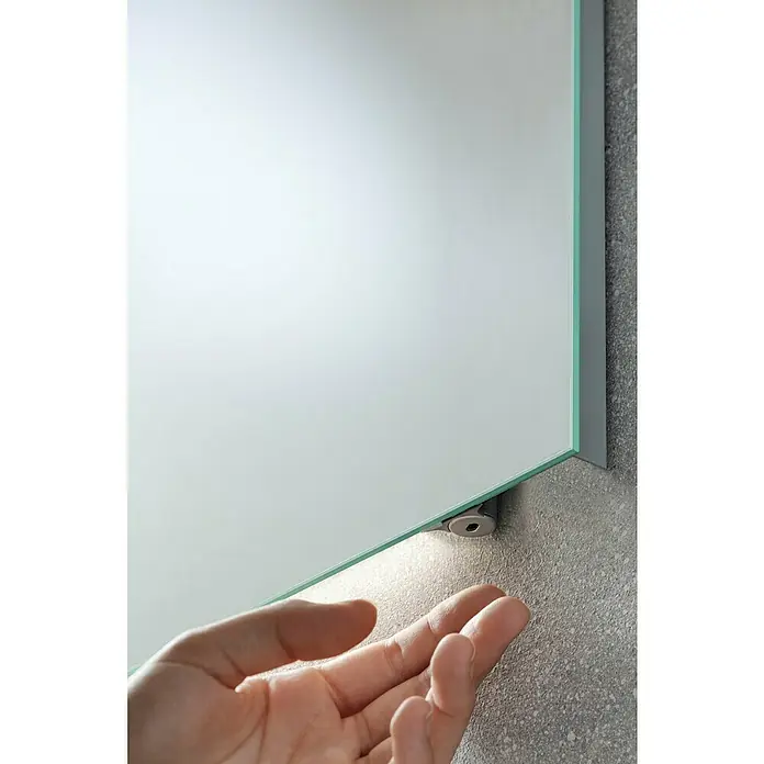 Fackelmann Mirrors LED-Lichtspiegel - 110 x 68 cm, Einfacher Anschluss über Schraubklemme, Rechteckig - Nahaufnahme eines Spiegels mit Rahmen und einer Hand, die nach dem Spiegel greift, wodurch die Beleuchtung des Spiegels hervorgehoben wird.