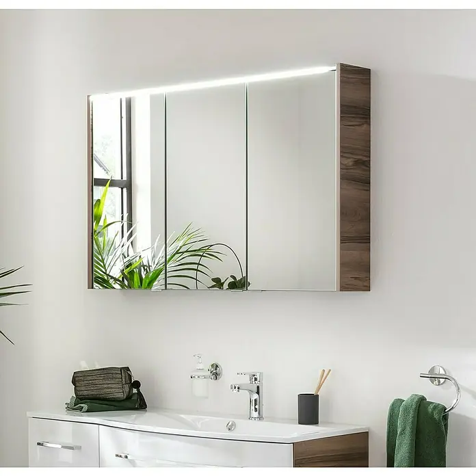 Fackelmann Verona LED-Spiegelschrank - 110 x 68,3 cm, Nussbaum Holzoptik - Ein stilvoller Spiegelschrank mit Holzrahmen und integrierter Beleuchtung über einem modernen Waschbecken im Badezimmer.