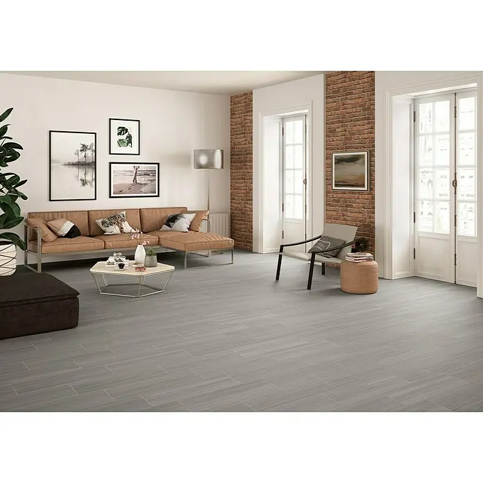Pavimento cerámico Ferik - 20,5 x 61,5 cm, Gris - Una amplia sala de estar con pisos de baldosas grises, un sofá marrón y detalles de paredes de ladrillo, creando un ambiente elegante y moderno.