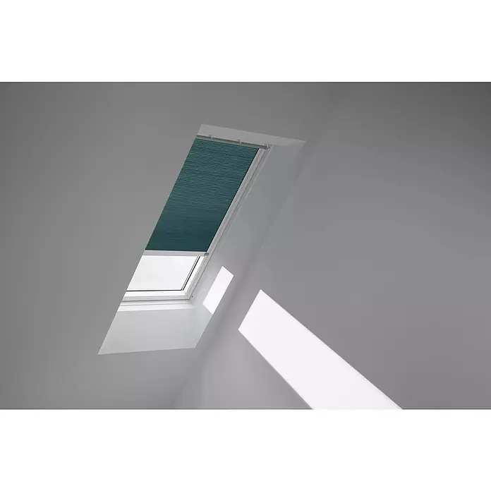 Velux Dachfensterplissee FSC M06 1173KWL - Farbe: Petrol - 1173KWL, Farbe Schiene: Weiß, Solarbetrieben - Das Bild zeigt ein Dachfenster mit einem Rollo in einem Raum mit weißen Wänden, das teilweise geöffnet ist, um Licht hereinzulassen.