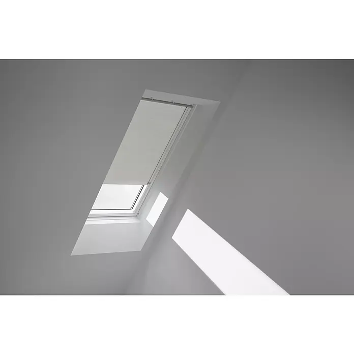 Velux Dachfensterplissee FSC P08 1172KWL - Farbe: Lichtgrau - 1172KWL, Farbe Schiene: Weiß, Solarbetrieben - Helles Dachfenster mit Jalousie in einem grauen Raum, das Licht und Schatten auf die Wand wirft und eine moderne Atmosphäre schafft.