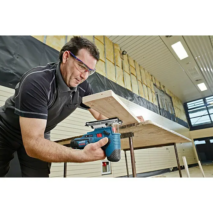 Bosch Professional Akku-Stichsäge GST 12V-70 L-Boxx - 12 V, Ohne Akku, Leerlaufhubzahl: 1.500 /min - 2.800 /min - Handwerker benutzt eine Bosch Stichsäge, um ein Holzbrett zu bearbeiten. Die blaue Stichsäge ist ein kabelloses Elektrowerkzeug.