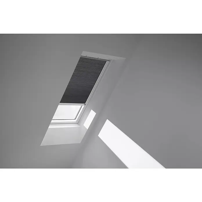 Velux Dachfensterplissee FMC UK04 1170KWL - Farbe: Grautaupe - 1170KWL, Farbe Schiene: Weiß, Elektrisch - Ein Dachfenster mit teilweise heruntergelassenem Rollo und hellem, indirektem Licht, das auf die Wand fällt.