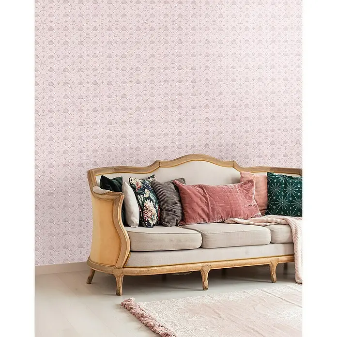 Glööckler Pompöös Provence Vliestapete - Rosa, Grafisch, 10,05 x 0,53 m - Blick auf eine Sofaecke mit einem zarten, rosa Hintergrundmuster und einem beige-farbenen Sofa, das mit verschiedenfarbigen Kissen dekoriert ist.