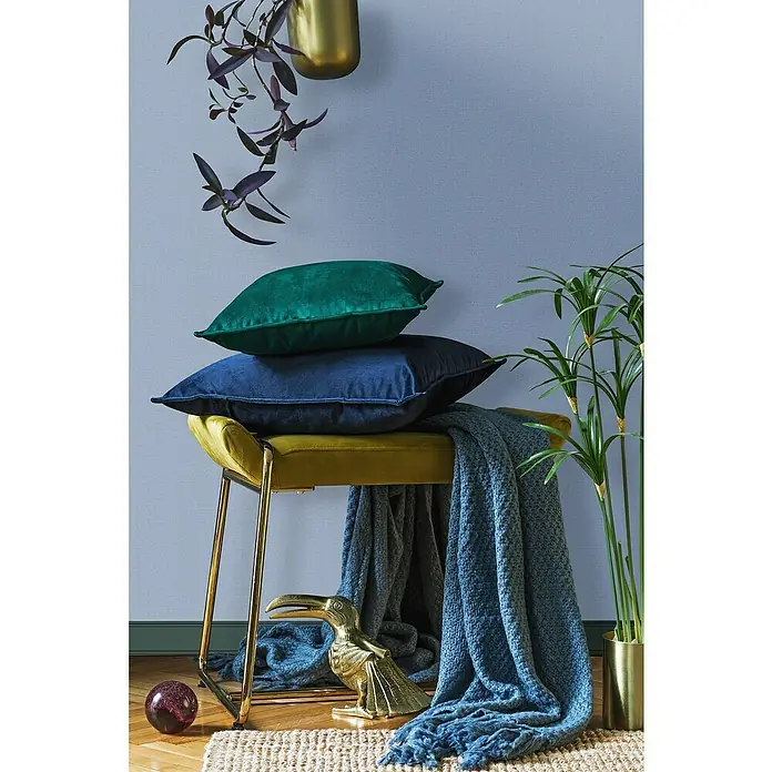 Glööckler Pompöös Provence Vliestapete - Blau, Uni, 10,05 x 0,53 m - Dekorative blaue und grüne Samtkissen auf einem gelben Hocker mit goldenen Beinen, ergänzt durch goldene Akzente und eine blaue Decke.