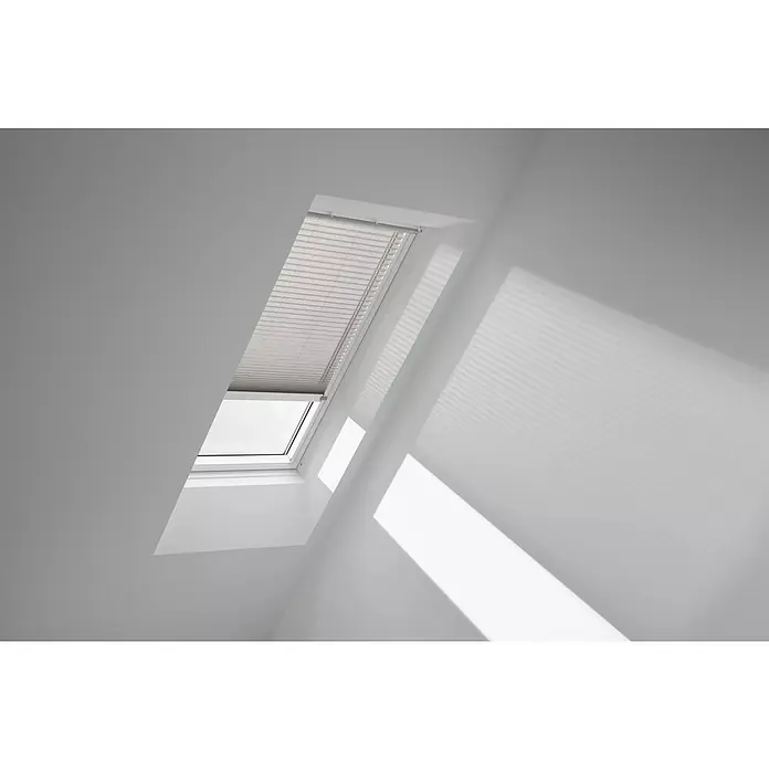 Velux Dachfensterplissee FML P10 1284KWL - Farbe: Silbergrau - 1284KWL, Farbe Schiene: Weiß, Elektrisch - Das Bild zeigt ein Dachfenster mit einem Rollo, das teilweise geschlossen ist, in einem hellen Raum, wobei das Licht interessante Schatten wirft.