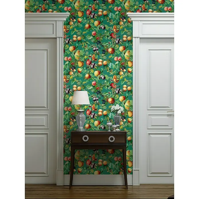 Glööckler Pompöös Provence Vliestapete - Grün/Orange, Floral, 10,05 x 0,53 m - Elegantes Interieur mit einer braunen Konsole, einer Lampe und Blumenvase vor einer grünen Tapete mit Fruchtmuster.