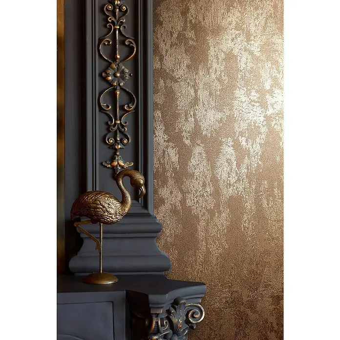 Glööckler Pompöös Provence Vliestapete - Kupfer, Metalloptik, 10,05 x 0,53 m - Detailaufnahme einer eleganten Wandgestaltung mit goldfarbener Texturtapete und dekorativem Kaminaufsatz mit Flamingo-Figur.