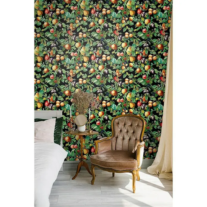 Glööckler Pompöös Provence Vliestapete - Schwarz/Grün/Orange, Floral, 10,05 x 0,53 m - Nahaufnahme eines Raumes mit einem bequemen Stuhl, einem Beistelltisch und einer Wand mit Obstgarten-Tapete.