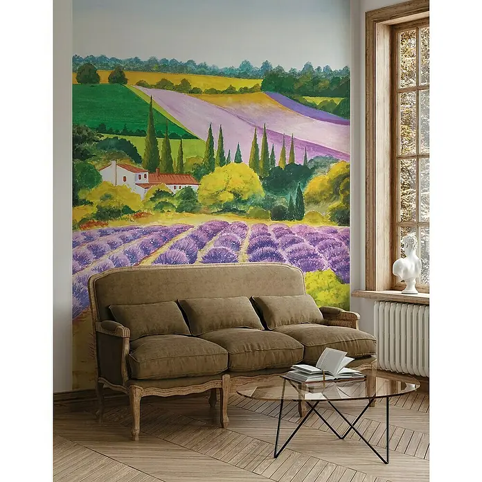 Glööckler Pompöös Provence Fototapete Malerische Lavendelfelder - B x L: 212 x 270 cm, Vlies - Wohnzimmer mit einer bequemen braunen Couch vor einer Wand mit Lavendel-Motiv und einem Couchtisch mit Büchern.