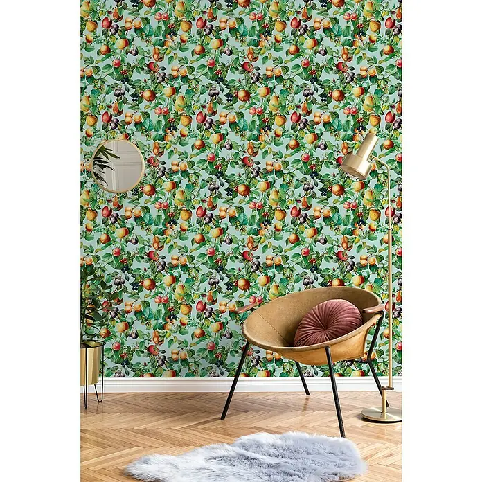 Glööckler Pompöös Provence Vliestapete - Blau/Grün/Orange, Floral, 10,05 x 0,53 m - Ein einladendes Interieur mit einem gemütlichen Sessel vor einer lebhaften Tapete, die mit Früchten und Blättern verziert ist.