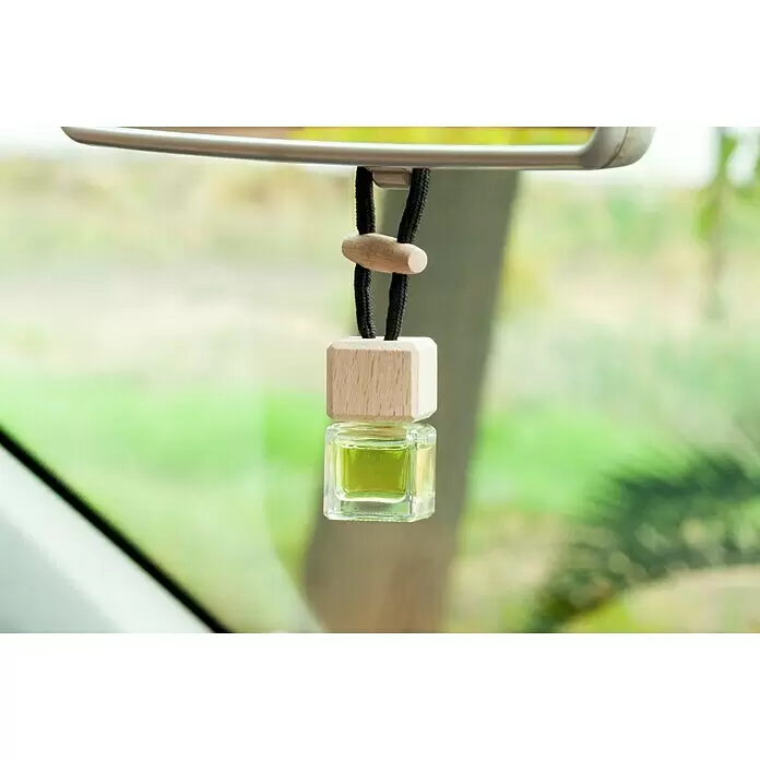 Ambientador de coche para colgar - Limón, 8 sem. - Ambientador de coche de cristal cuadrado con líquido verde y tapa de madera clara, colgando de un espejo retrovisor.