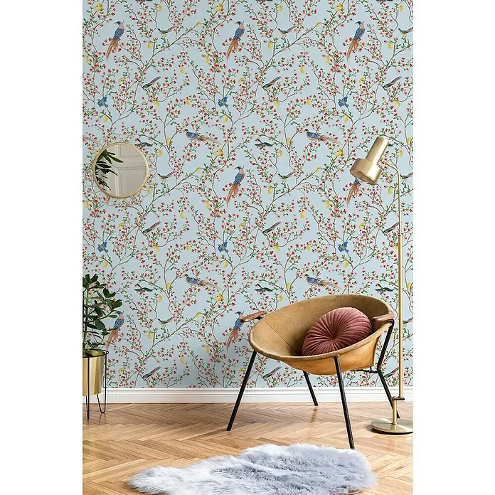 Glööckler Pompöös Provence Vliestapete - Blau/Grün/Rot, Floral, 10,05 x 0,53 m - Stilvolles Interieur mit floraler Wandtapete, Sessel und Stehlampe. Die blumige Tapete bildet einen schönen Hintergrund für das Möbelarrangement.