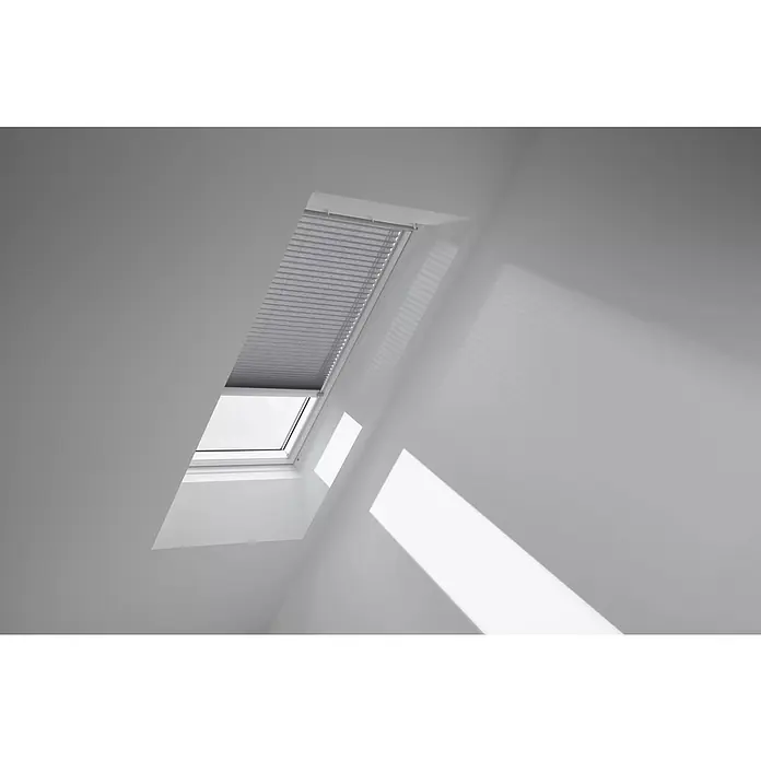 Velux Dachfensterplissee FSL F06 1282K - Farbe: Grau - 1282K, Farbe Schiene: Aluminium, Solarbetrieben - Ein Dachfenster mit einem Rollo, das teilweise heruntergezogen ist und Licht in einen weißen Raum lässt.