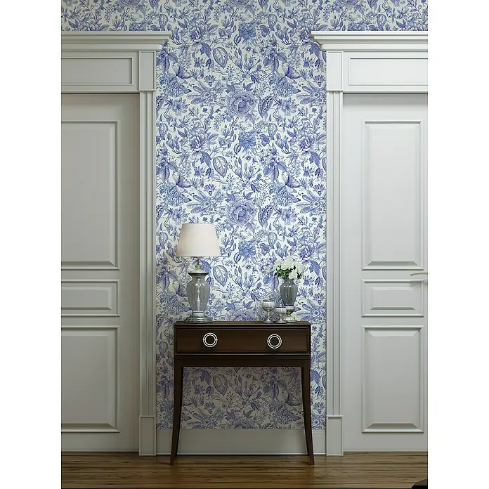 Glööckler Pompöös Provence Vliestapete - Weiß/Blau, Floral, 10,05 x 0,53 m - Stilvolle Ansicht eines Raumes mit blau-weiß gemusterter Tapete, einem dunklen Holzschrank, einer Lampe und weißen Türen.