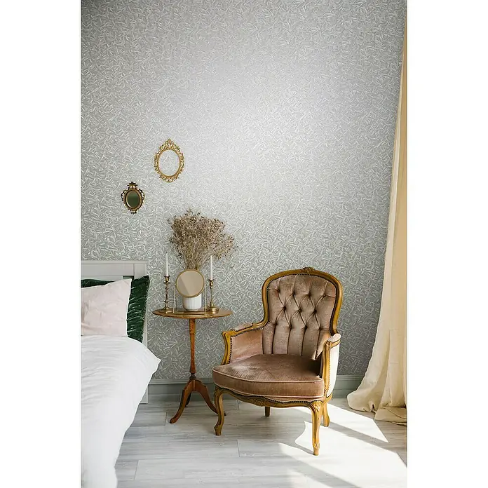 Glööckler Pompöös Provence Vliestapete Basic - Pearl, Floral, 10,05 x 0,7 m - Eleganter Sessel mit Samtbezug und Goldrahmen, kombiniert mit stilvollen Vintage-Accessoires in einem Schlafzimmer mit gemusterter Tapete.