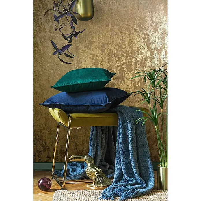 Glööckler Pompöös Provence Vliestapete - Gold, Metalloptik, 10,05 x 0,53 m - Dekoratives Arrangement mit Zierkissen in Blau- und Grüntönen auf einem goldenen Hocker, ergänzt durch eine blaue Decke und goldene Akzente.