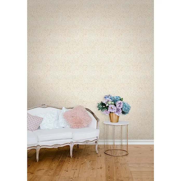 Glööckler Pompöös Provence Vliestapete - Beige/Braun, Ornament, 10,05 x 0,53 m - Elegante weiße Couch mit Zierkissen und Blumenarrangement auf einem Beistelltisch, vor einer stilvollen Tapete.